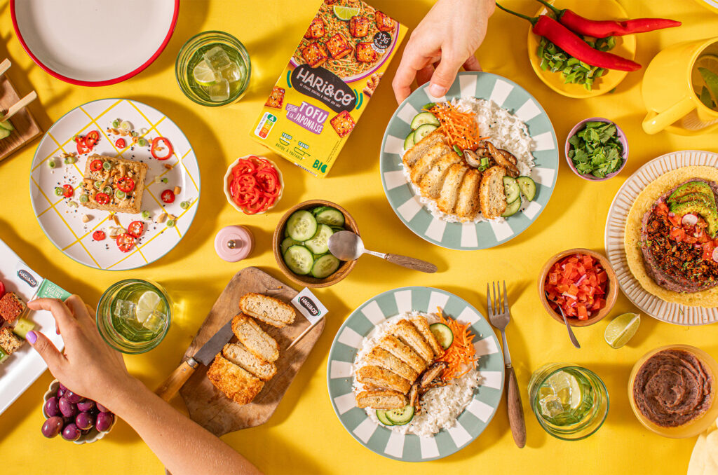 Assiettes de tofu pané avec riz et légumes, autour d’un paquet HARi&CO sur une table jaune.