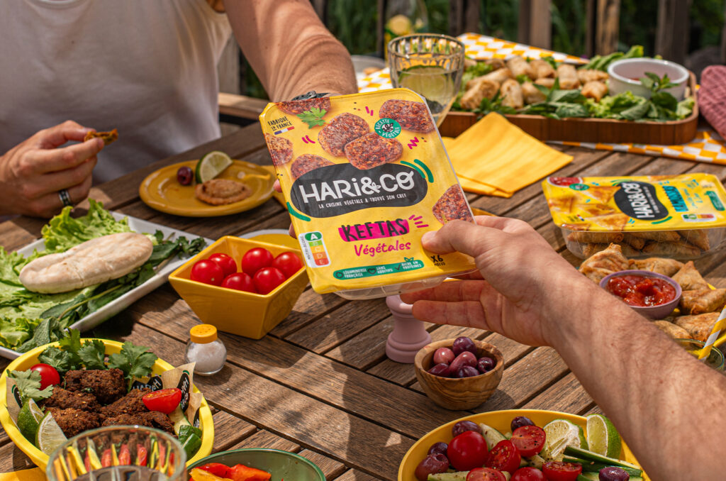 Un paquet de keftés végétales HARi&CO tenu au-dessus d’une table d’apéritif.